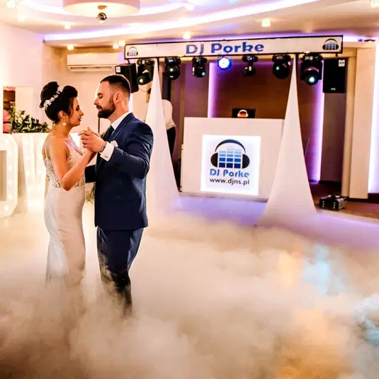  Pierwszy taniec młodej pary na weselu prowadzonym przez DJ-a, parkiet w mgiełce, ślubna sala udekorowana światłami. 