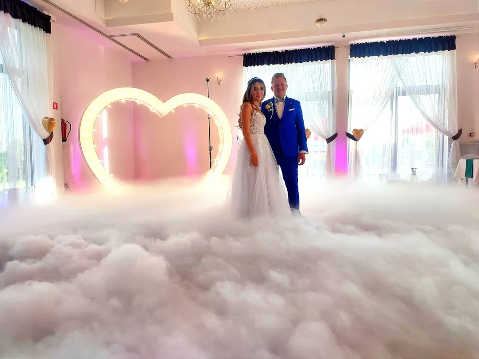 Para młoda na weselu w otoczeniu dymu, dekoracja w kształcie serca, eleganckie wnętrze, romantyczna atmosfera.