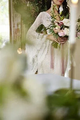 Panna młoda w koronkowej sukni trzyma bukiet kwiatów na romantycznym ślubie, elegancka kompozycja weselna.