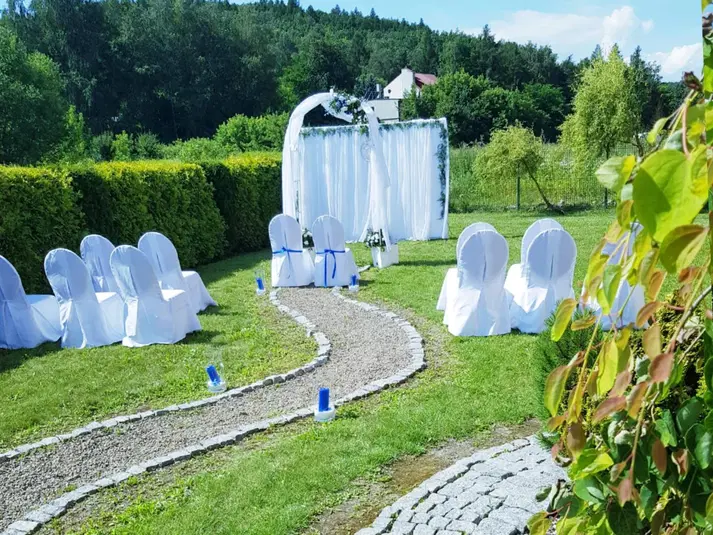  Plenerowa ceremonia ślubna z białymi krzesłami i altaną, otoczona zielenią w ogrodzie. 