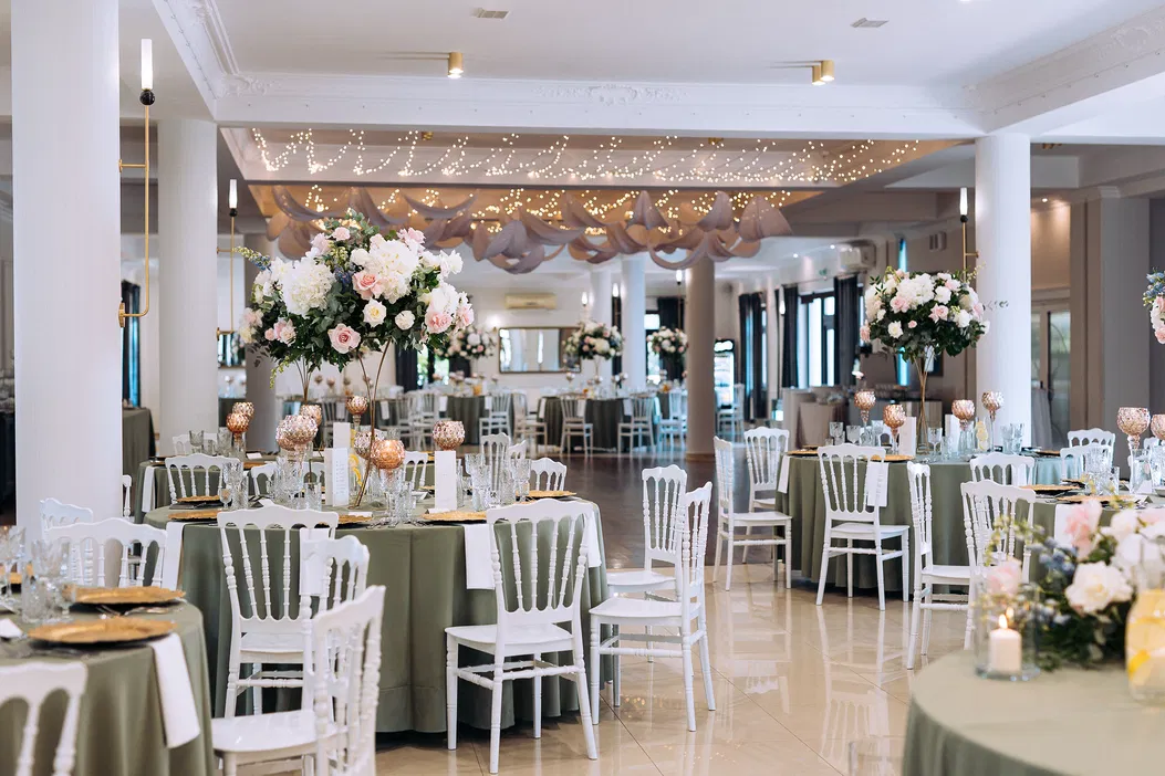Elegancka sala weselna z dekoracjami kwiatowymi, okrągłymi stołami i białymi krzesłami.