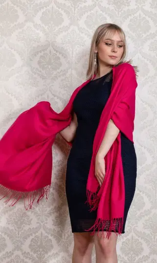  Kobieta w eleganckiej czarnej sukience z różowym szalem, stojąca na tle wzorzystej tapety. 
