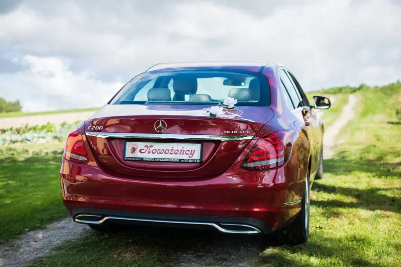  Czerwony Mercedes C200d udekorowany na ślub, widok z tyłu na tablicę rejestracyjną Nowożeńcy na wiejskiej drodze. 