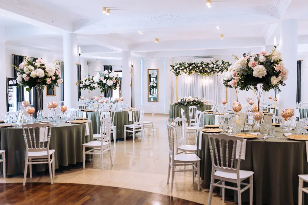 Elegancka sala weselna z dekoracjami kwiatowymi, zielonymi obrusami i białymi krzesłami, idealna na przyjęcie weselne.