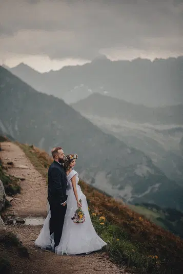  Para młoda w górach, sesja ślubna w plenerze, suknia ślubna i garnitur, romantyczna scena na tle górskiego krajobrazu, fotografia ślubna na szlaku turystycznym, bukiet kwiatów, wianek z kwiatów. 