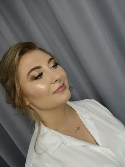  Nie wiem, kto jest na zdjęciu, ale optymizowany alt tekst może być taki: Kobieta z eleganckim makijażem, blond włosy, biała koszula, pozowanie na tle szarej zasłony. 