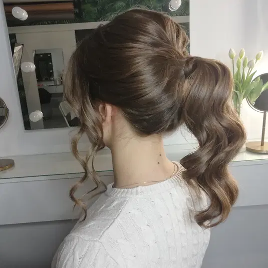  Damska fryzura na kucyk z eleganckimi lokami, widok z tyłu, stylizacja włosów w salonie, modne upięcie do ramion. 