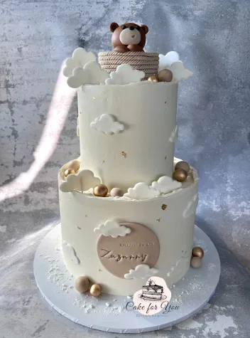Dwupiętrowy tort dekorowany chmurkami, z misiem na szczycie. Idealny na przyjęcie dla dzieci lub baby shower.