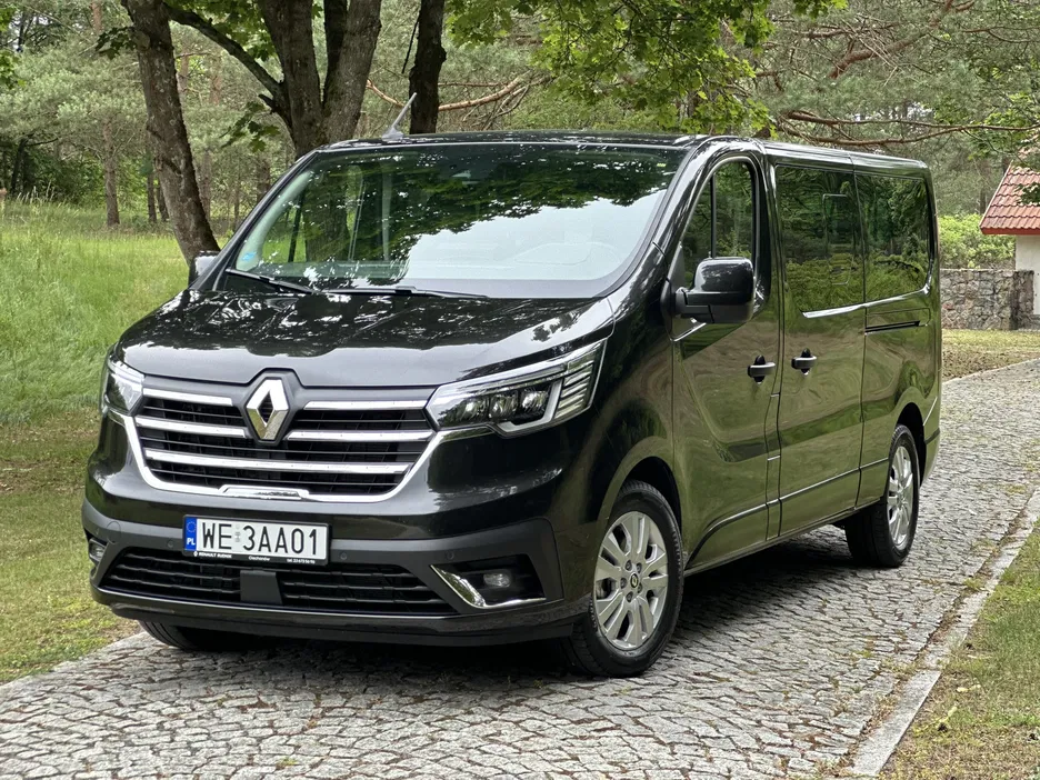 Czarny van Renault Trafic zaparkowany na brukowanej drodze w lesie.