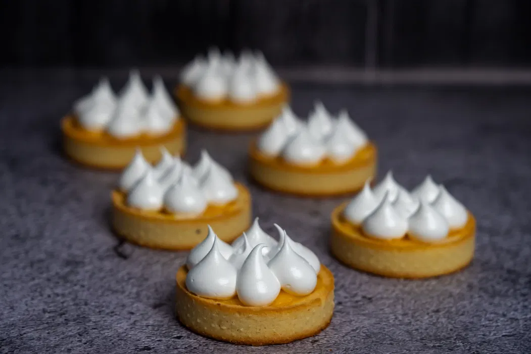 Sześć mini tart cytrynowych z bezą na szarej powierzchni.
