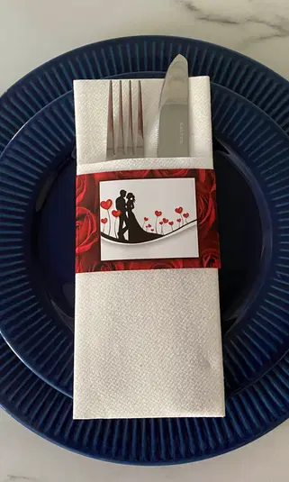  Zestaw sztućców na przyjęcie weselne, elegancko ułożony na granatowym talerzu; dekoracja z motywem pary młodej i serc. 