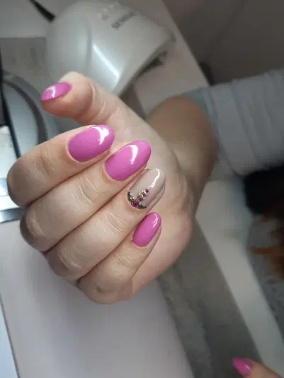  Nail art manicure with pink and nude colors, featuring colorful rhinestones, in a beauty salon setting. 