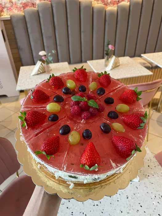 Tort owocowy z truskawkami, winogronami i malinami na złotej paterze, w eleganckim wnętrzu kawiarni.