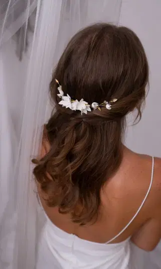  Elegancka fryzura ślubna z ciemnymi falami i delikatną ozdobą z białych kwiatów, widok od tyłu, welon i suknia ślubna. 