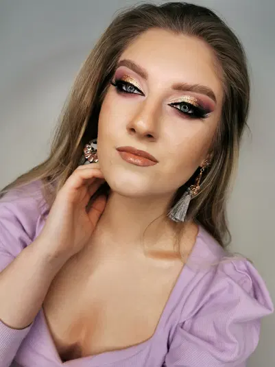  Kobieta z makijażem glamour, złote cienie do powiek, fioletowa bluzka, eleganckie kolczyki 