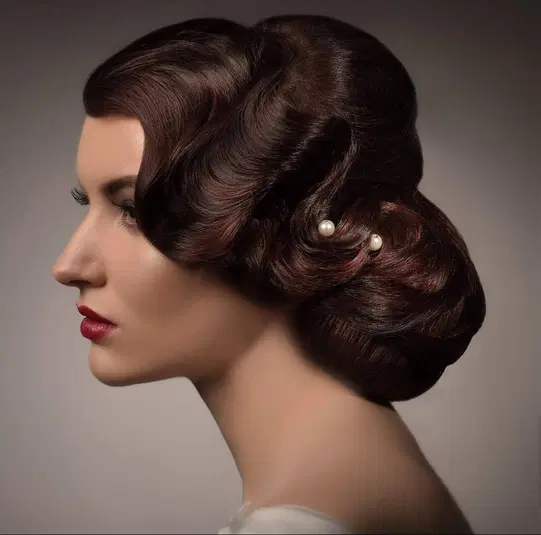  Elegancka fryzura vintage z falami, ozdobiona perłowymi spinkami, profil kobiety z czerwoną szminką na ustach. 