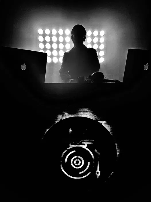 DJ podczas występu na żywo, efektowne oświetlenie, scena z laptopami marki Apple, czarno-biała fotografia.