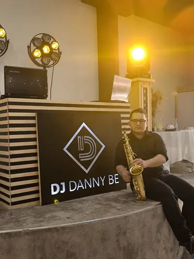  DJ na scenie z saksofonem, oświetlenie sceniczne, logo DJ Danny Be. 