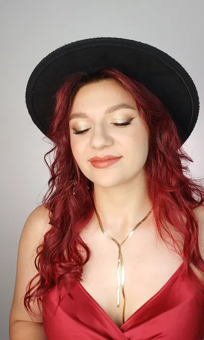 Czarna kapelusz, złoty makijaż oczu, czerwona sukienka, błyszczący naszyjnik, styl glamour.