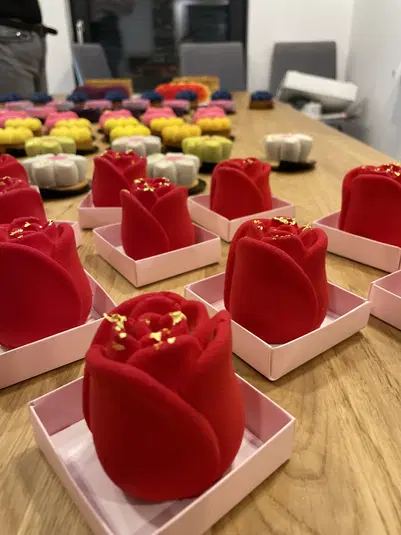  Deser w kształcie czerwonych róż na drewnianym stole, otoczony kolorowymi mini ciastkami, idealny na eleganckie przyjęcie lub degustację. 